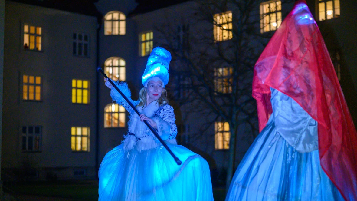 Stelzentänzerinnen mit beleuchteten Kostümen bei Nacht im Innenhof des Hauses Heilig Geist