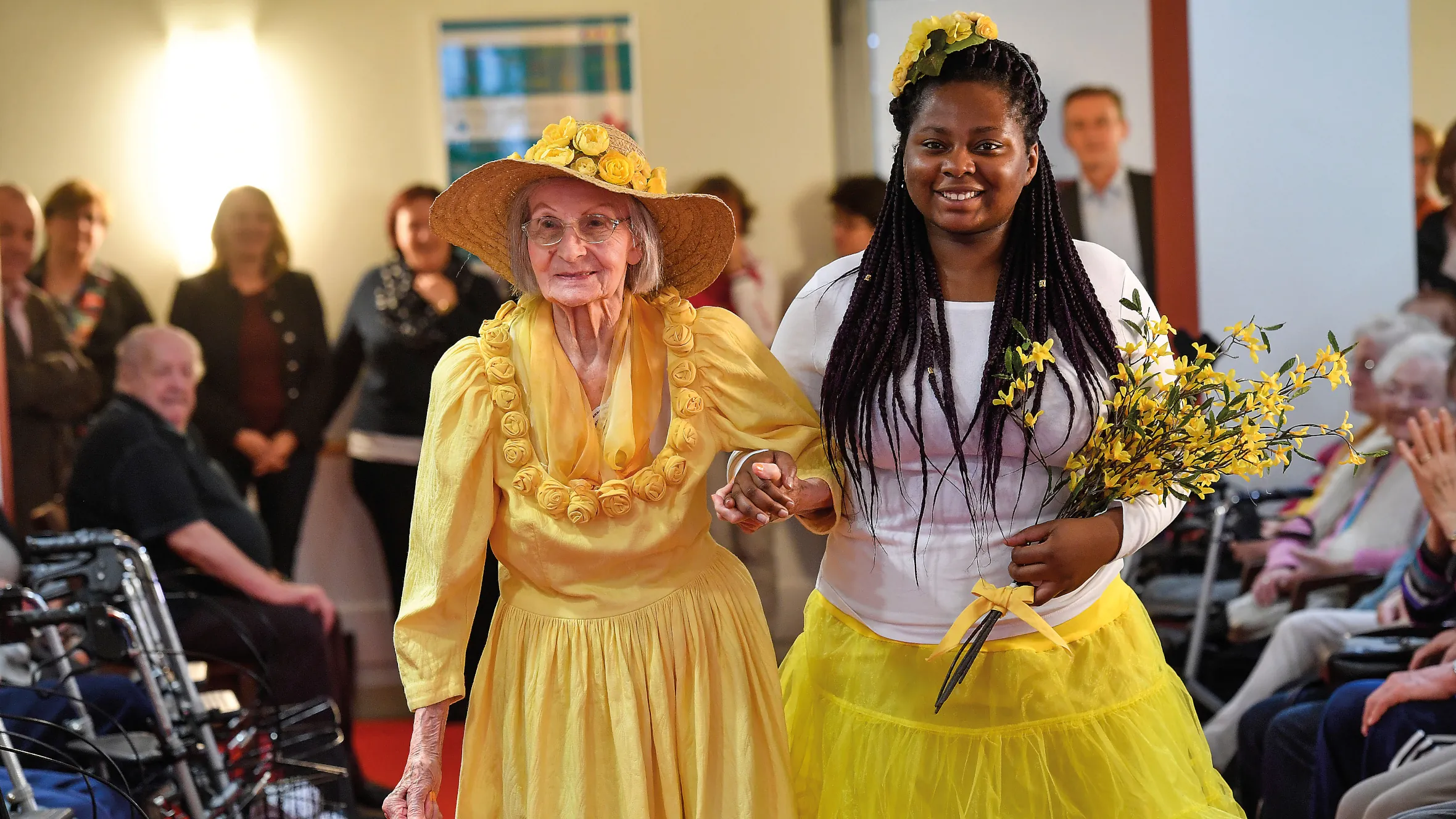 Resident with yellow dress and big hat at the residence’s annual fashion show