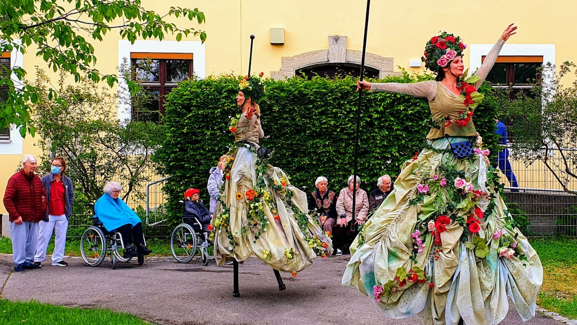 Stelzentänzerinnen mit blumigen Kostümen im Garten des Hauses an der Rümannstraße
